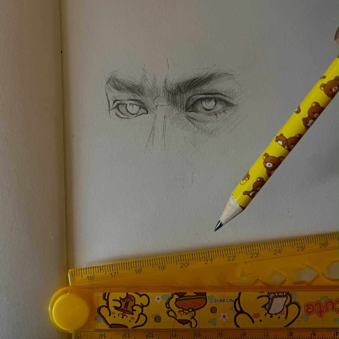 Graphite drawing of eyes beside a yellow pencil and ruler
